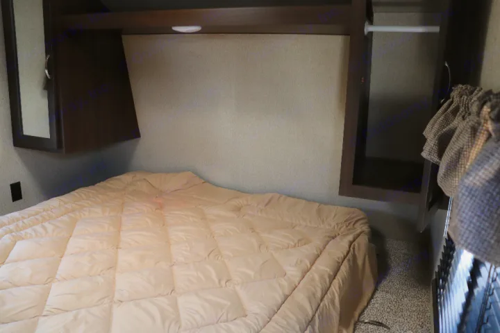 Cozy RV rental bedroom features a comfortable bed, overhead cabinets, and a wardrobe, optimizing travel space.. Keystone Springdale 2020