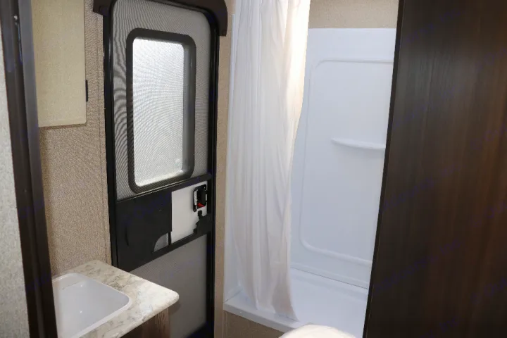 RV rental bathroom interior with a white sink, a white shower stall and curtain, and an RV screen door.. Keystone Springdale 2020