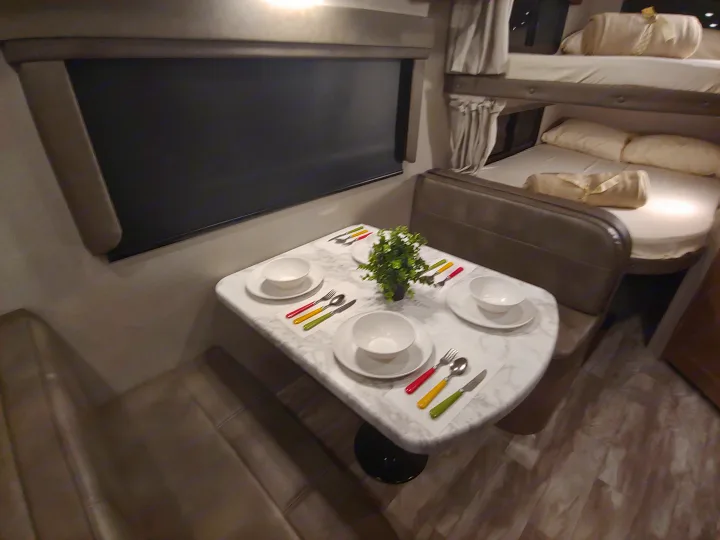 Bright rv rental interior featuring a marble-patterned dinette table with place settings, next to cozy bunk beds.. Grand Design Imagine XLS 21BHE 2020
