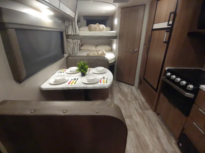 RV rental interior: dinette set for four, compact kitchen (stove, fridge), and cozy bunk beds visible.. Grand Design Imagine XLS 21BHE 2020
