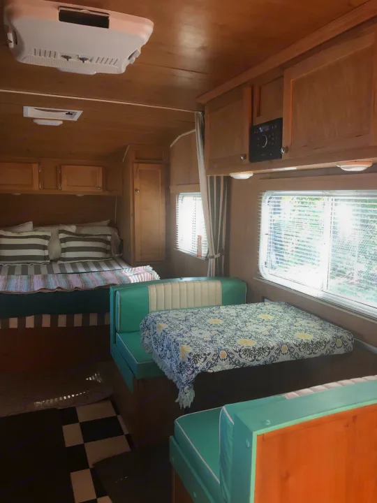 RV rental interior featuring a cozy bed, dinette with teal cushions, wooden cabinets, and an AC unit. Perfect for your next adventure.. Riverside Rv 189R Retro 2018