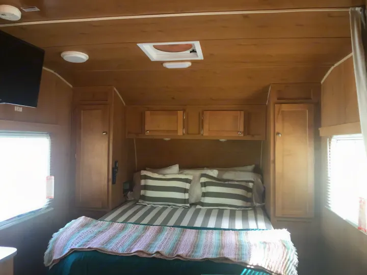 Cozy rv rental bedroom features a comfortable bed, wood walls, ample storage, and TV. Ideal for your mobile adventures.. Riverside Rv 189R Retro 2018