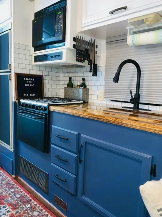 Modern RV rental kitchen with blue cabinets, wood counter, white tile backsplash, microwave, stove, and sink. Functional space.. Fleetwood Flair 1997