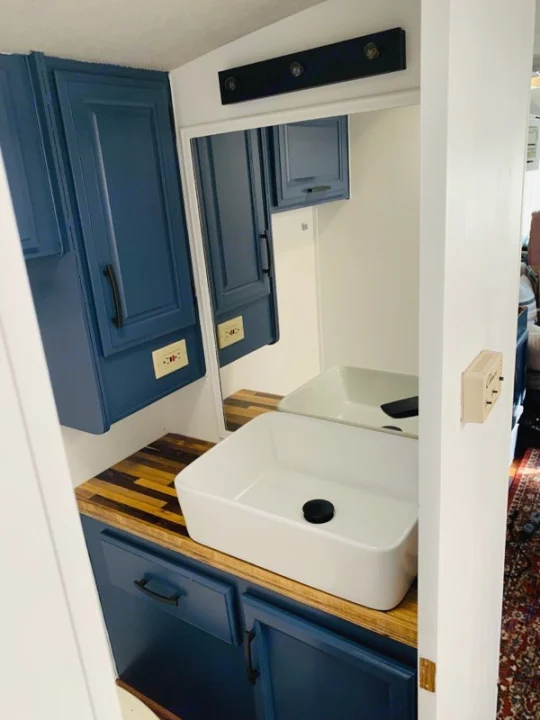 Modern RV rental bathroom vanity with blue cabinets, wood counter, white vessel sink, mirror, and lights. Compact & stylish.. Fleetwood Flair 1997