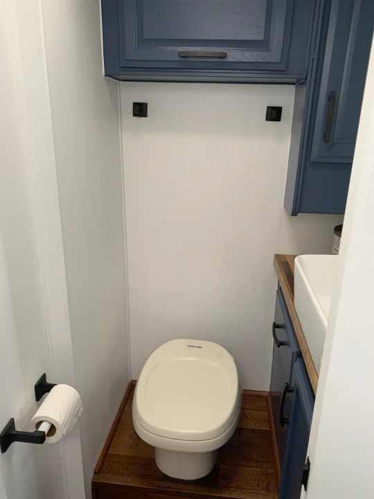 RV rental bathroom: white Thetford toilet, navy cabinets, and a white sink with black hardware and wood accents.. Fleetwood Flair 1997