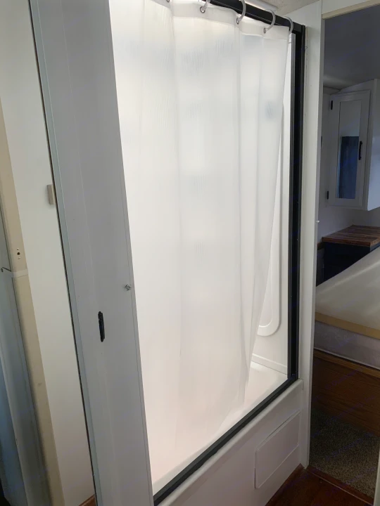 Compact RV shower with translucent curtain, part of a functional RV rental interior. Features nearby bedroom area.. Fleetwood Flair 1997