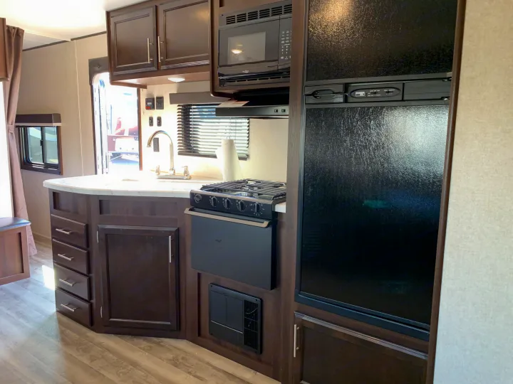 Modern rv rental kitchen featuring dark cabinets, a sink, stove, microwave, and refrigerator for comfortable road trips.. Jayco Jay Flight 2019