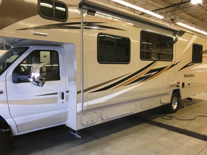 Side view of a beige Winnebago Minnie Winnie Class C RV rental, detailing its graphics, extended awning, and storage compartments.. Winnebago Minnie Winnie 2019