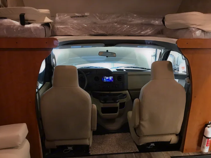 RV rental interior: Driver's cab and overhead bed with new, plastic-wrapped cushions. A fire extinguisher is visible on the right.. Winnebago Minnie Winnie 2019