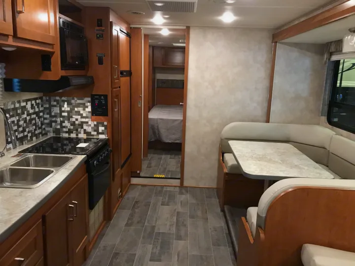 Spacious RV rental interior featuring a full kitchen, dining booth, and a view into the cozy bedroom.. Winnebago Minnie Winnie 2019