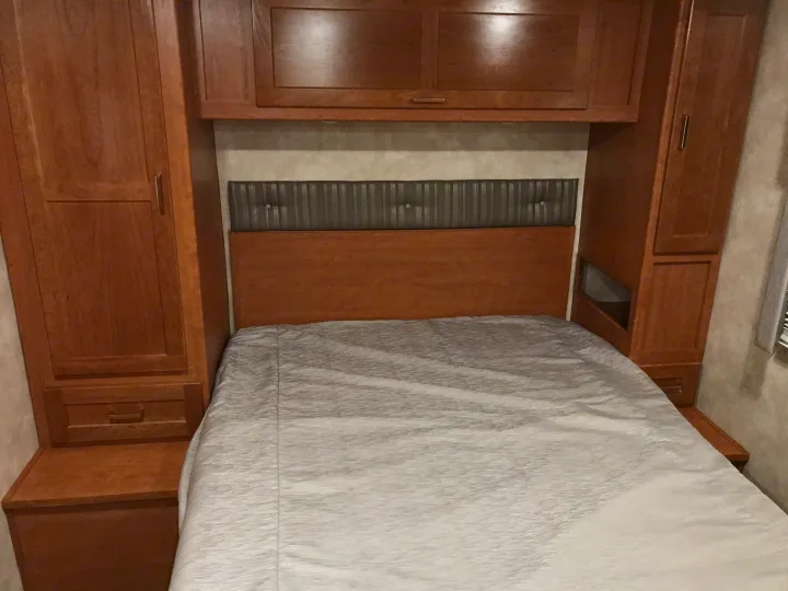 Compact RV rental bedroom featuring built-in wood cabinets, an upholstered headboard, and cozy grey bedding.. Winnebago Minnie Winnie 2019