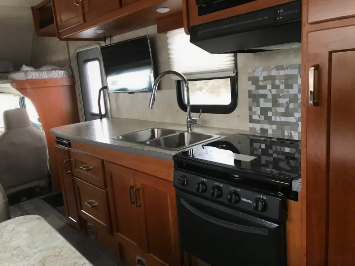 Inside a modern RV rental: a well-equipped kitchen with sink, stove, and TV, plus a cozy cab-over sleeping area.. Winnebago Minnie Winnie 2019