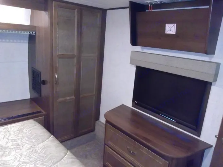 Cozy RV rental bedroom featuring a bed, wood-toned wardrobe, wall-mounted TV, and dresser for storage.. Highland Ridge Mesa Ridge 427BHS 2019