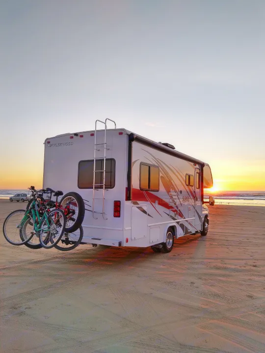This RV rental, equipped with bikes, offers a perfect beach adventure at sunset, with golden light reflecting on the sand and ocean waves.. Fleetwood Other 2018