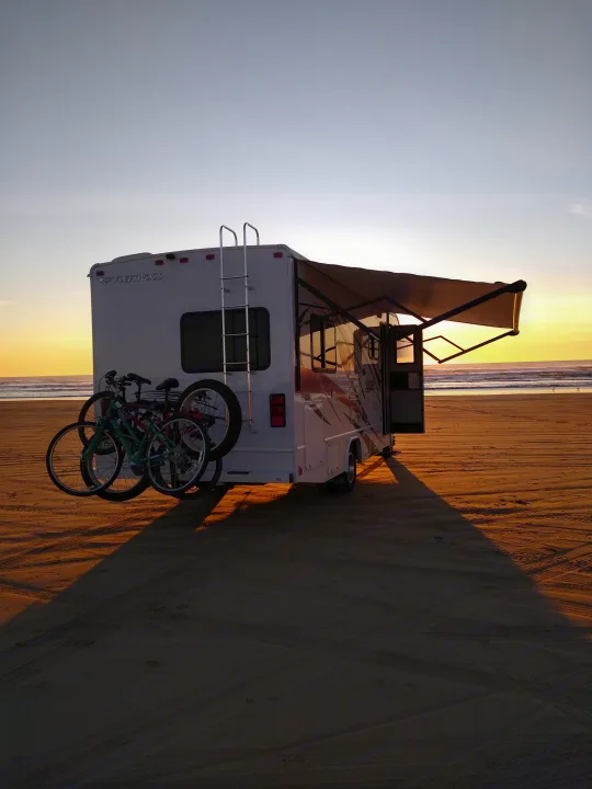 RV rental on a golden sandy beach at sunset, bikes attached, awning extended, ocean waves beyond. Perfect travel scene.. Fleetwood Other 2018
