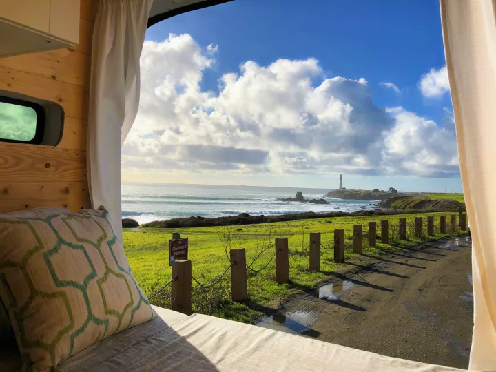 Coastal panorama from an RV rental: lighthouse, ocean waves, and green fields. Interior visible with a 'No Overnight Parking' sign outside.. Ford Transit 2015