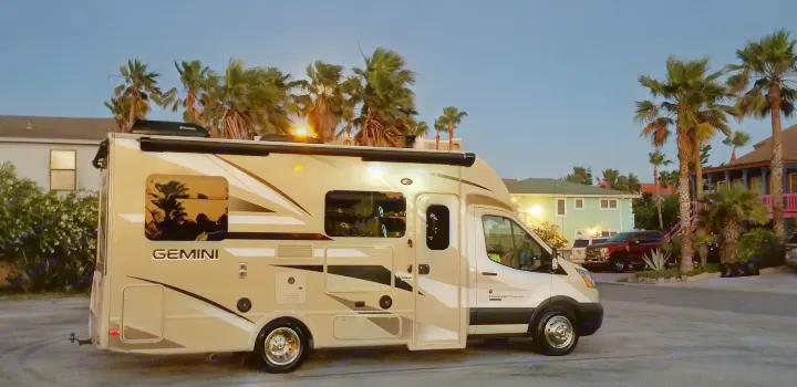 A modern tan & white Gemini RV rental is parked at dusk, with swaying palm trees & coastal homes in the background.. Thor Motor Coach Gemini 2016