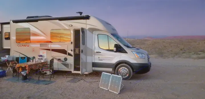 RV rental in the desert at dusk. Sunset reflections in windows, solar panels charging, and a camping setup.. Thor Motor Coach Gemini 2016