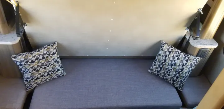 Cozy RV rental interior: gray dinette seating with two geometric pillows and wall-mounted convertible bed hardware.. Thor Motor Coach Gemini 2016