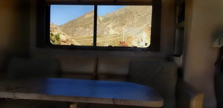 Cozy RV rental interior, featuring a table & sofa, with a panoramic window view of desert mountains. Adventure awaits!. Thor Motor Coach Gemini 2016