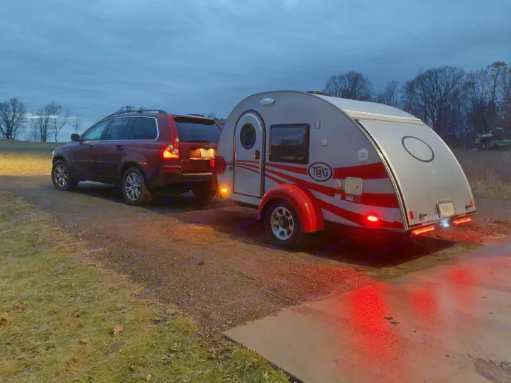 Red SUV tows a T@G teardrop camper (RV rental) at twilight on a dirt path with tail lights glowing.. T@G T@G Trailer 2016