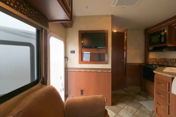 Explore this RV rental's cozy interior: a kitchen, living area with TV, and main entrance.. Thor Motor Coach Freedom Elite 2013