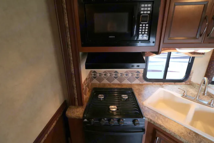 Compact RV rental kitchen featuring a microwave, gas stovetop, sink, and counter space for preparing meals.. Thor Motor Coach Freedom Elite 2013