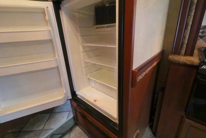 Open RV rental refrigerator, showcasing a clean, empty interior with shelves and door storage, ready for your next adventure's food.. Thor Motor Coach Freedom Elite 2013