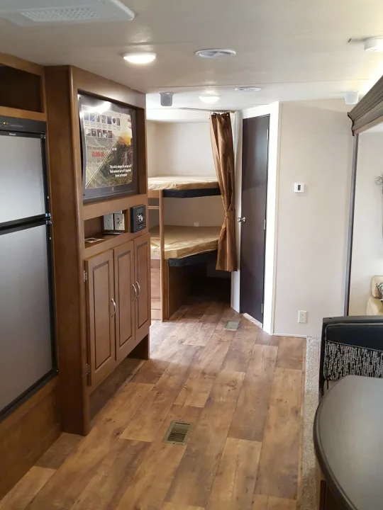 Spacious RV rental interior: living area with TV, integrated kitchen, and private bunk beds for travel comfort.. Forest River Wildwood 27DBK 2017