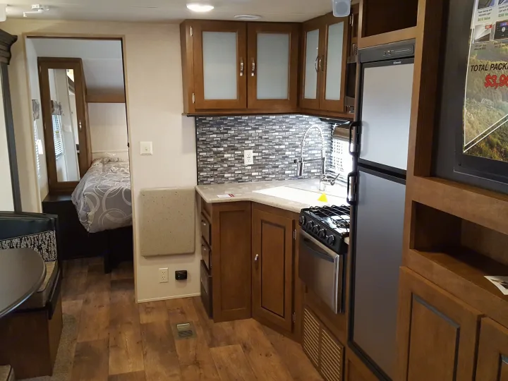 Inside an RV rental: a modern kitchen with backsplash, sink, stove, fridge, leading to a cozy bedroom.. Forest River Wildwood 27DBK 2017