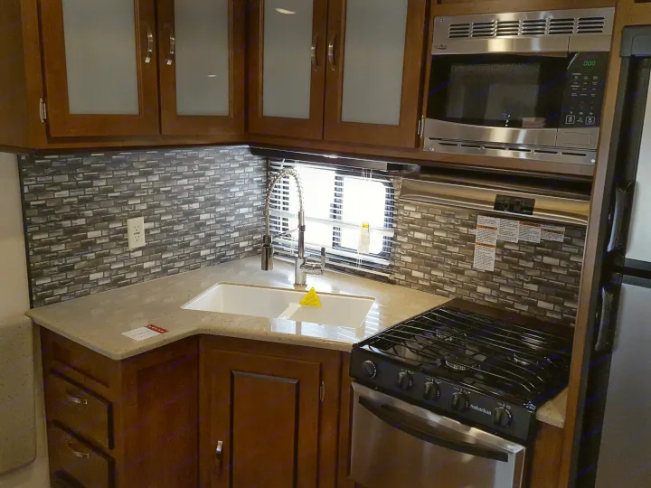 Explore this RV rental kitchen: L-shaped counter, modern cabinets, microwave, sink, and gas stove for cooking.. Forest River Wildwood 27DBK 2017