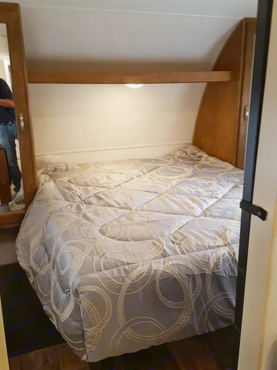 RV rental interior: A comfortable bedroom setup with patterned comforter, built-in shelving, and accent lighting.. Forest River Wildwood 27DBK 2017