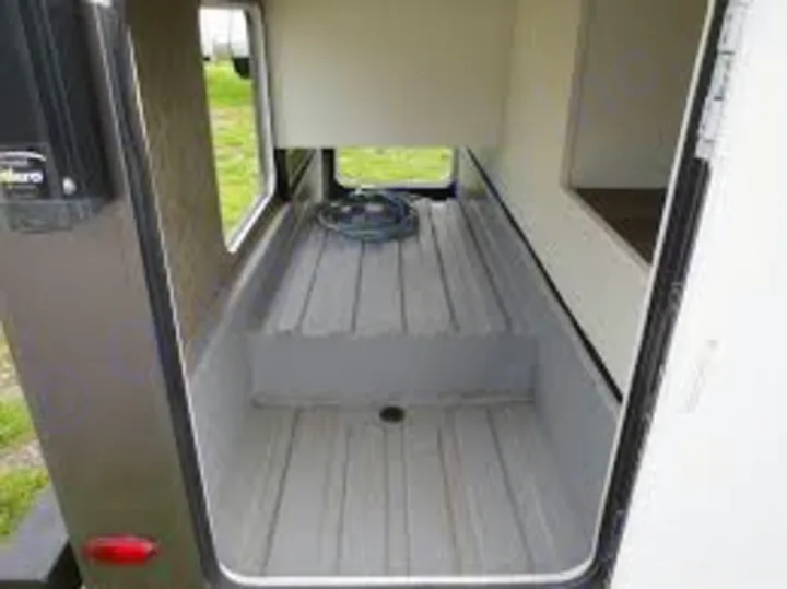 An open, spacious pass-through storage bay in an RV rental, showing ribbed flooring and a coiled hose.. Forest River Forester 2018