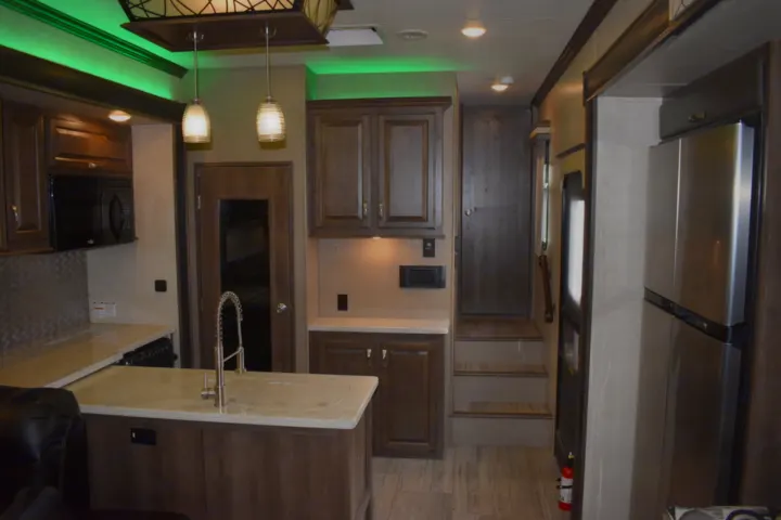 Modern RV rental interior features a full kitchen, island, stainless steel fridge, and steps to a living area.. K-Z Manufacturing Venom 2017