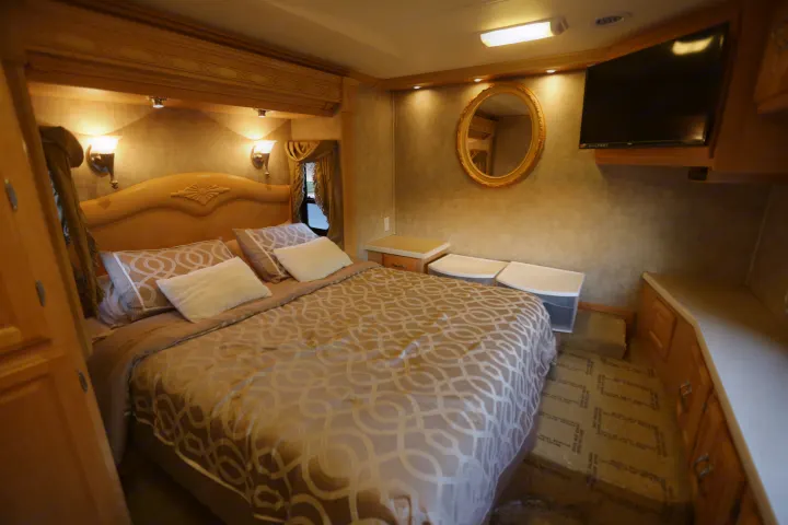 Spacious RV rental bedroom featuring a cozy bed, TV, built-in storage, and warm lighting for comfortable travel.. Coachmen Cross Country 2005