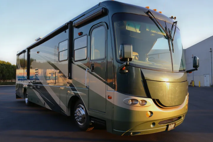 A large, two-tone green and beige luxury RV is parked on asphalt, illuminated by warm sunlight, perfect for an RV rental adventure.. Coachmen Cross Country 2005