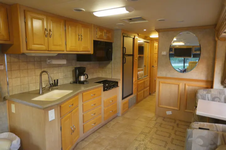 RV rental interior: well-equipped kitchen with wood cabinets, sink, stovetop, microwave, fridge, and cozy living area.. Coachmen Cross Country 2005