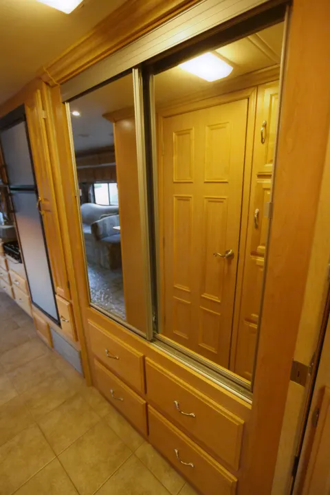 RV rental interior with mirrored closet doors, warm wood cabinetry, and tiled floor. A living area is reflected.. Coachmen Cross Country 2005