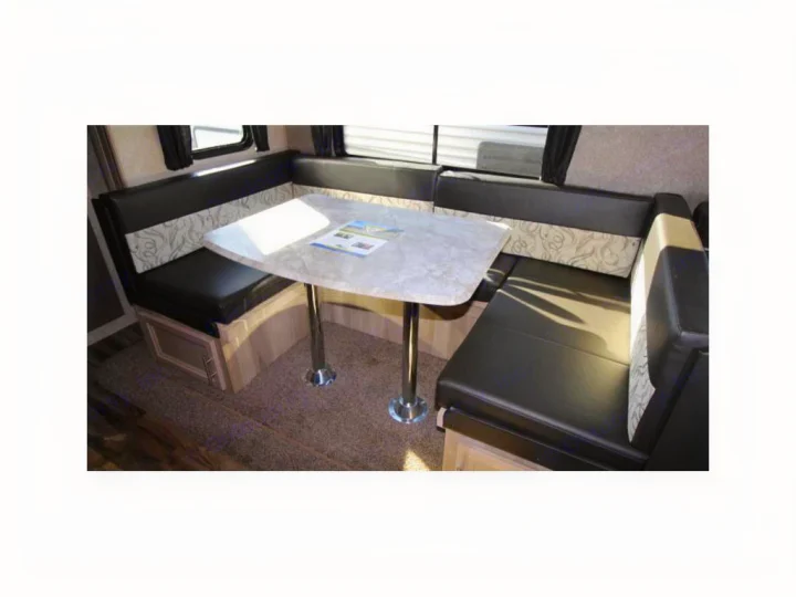 Inside an RV rental: a cozy L-shaped dinette featuring black cushioned seating with patterned accents and a sturdy table.. Coachmen Catalina 2019