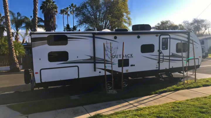 White travel trailer RV rental, an Outback Ultralite, parked on a residential street under a clear sky.. Keystone Outback 2019