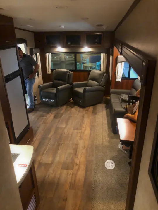 Inside a comfortable RV rental living space, featuring recliners, sofa, and kitchen area, with two occupants.. Jayco Eagle Super Lite 2018