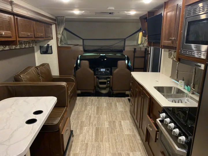 Interior of a modern RV rental, featuring a full kitchen, living space, and driver's cockpit with an overhead bunk.. Forest River Forester 2020