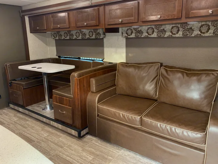 Cozy RV rental interior featuring a dinette with brown booth seating, a matching sofa, and overhead wood cabinets.. Forest River Forester 2020
