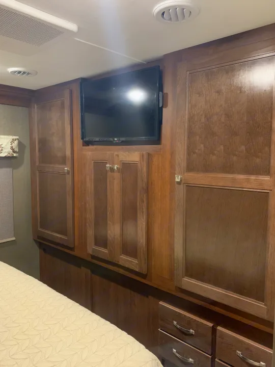 An RV rental's bedroom showcasing rich dark wood cabinetry, a wall-mounted TV, and a quilted bed.. Forest River Forester 2020