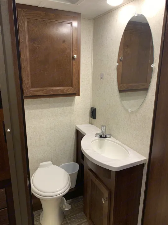 This RV rental bathroom offers a compact toilet, sink, vanity, oval mirror, and wall cabinet—essential for comfortable travel.. Forest River Forester 2020