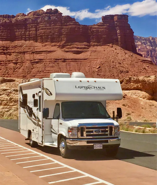 This RV rental is parked against a backdrop of stunning red rock cliffs under a blue sky, showcasing a scenic journey.. Forest River Coachmen Leprechaun 2014