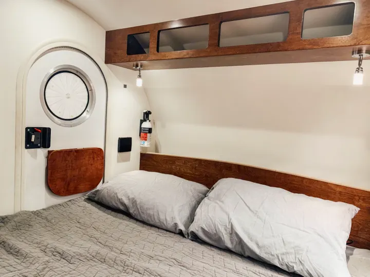 Comfortable RV rental bedroom with a cozy bed, wooden overhead storage, and a unique circular door in a compact camper interior.. T@G T@G Trailer 2016