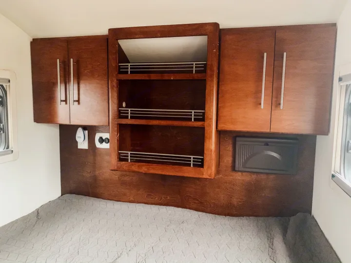 RV rental interior: cozy bedroom with dark wood cabinets, central open shelving, and a grey quilted bed. Functional small space.. T@G T@G Trailer 2016