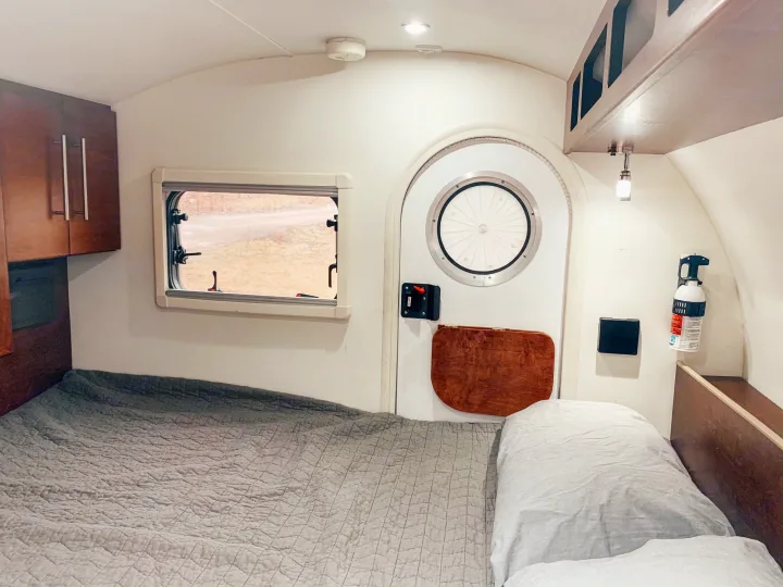 Interior of a compact RV rental bedroom, featuring a large bed, wooden cabinets, and a distinctive round entry door.. T@G T@G Trailer 2016