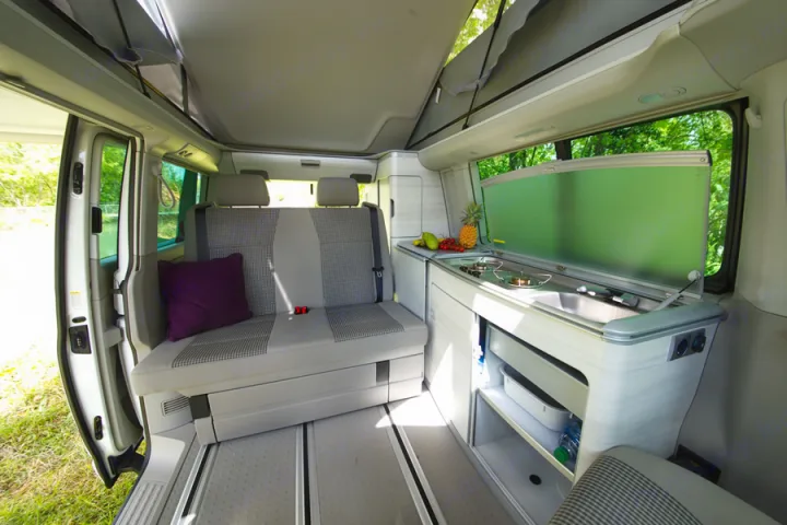 Experience the cozy interior of this camper van rv rental, featuring a kitchen, seating, and pop-top roof for your next adventure.. Volkswagen California Coast T6 2021